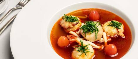 Un plato blanco con un guiso de mariscos, que incluye mejillones y camarones, adornado con hierbas.