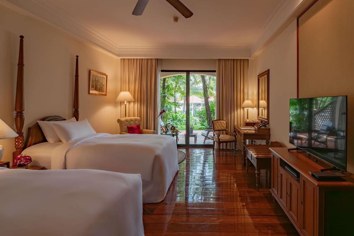 A hotel room with two beds, a desk with a chair, a television, and a large window with curtains.