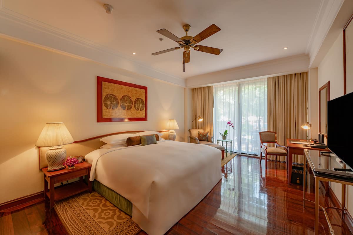 A hotel room with a large bed, a ceiling fan, a desk with a TV, and a window with curtains.