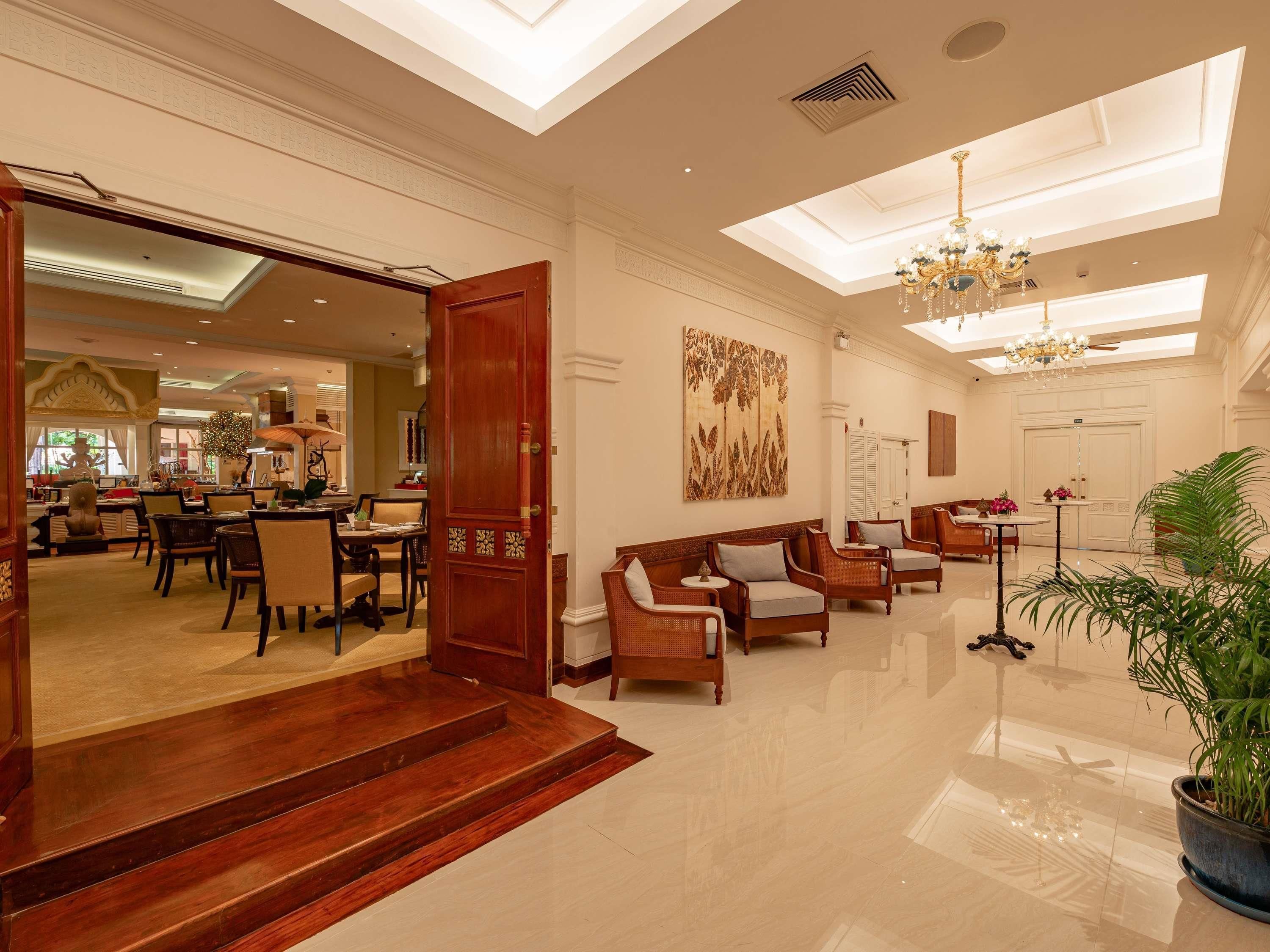 A spacious lobby with a high ceiling, a grand chandelier, and a large wooden door leading to a dining area.