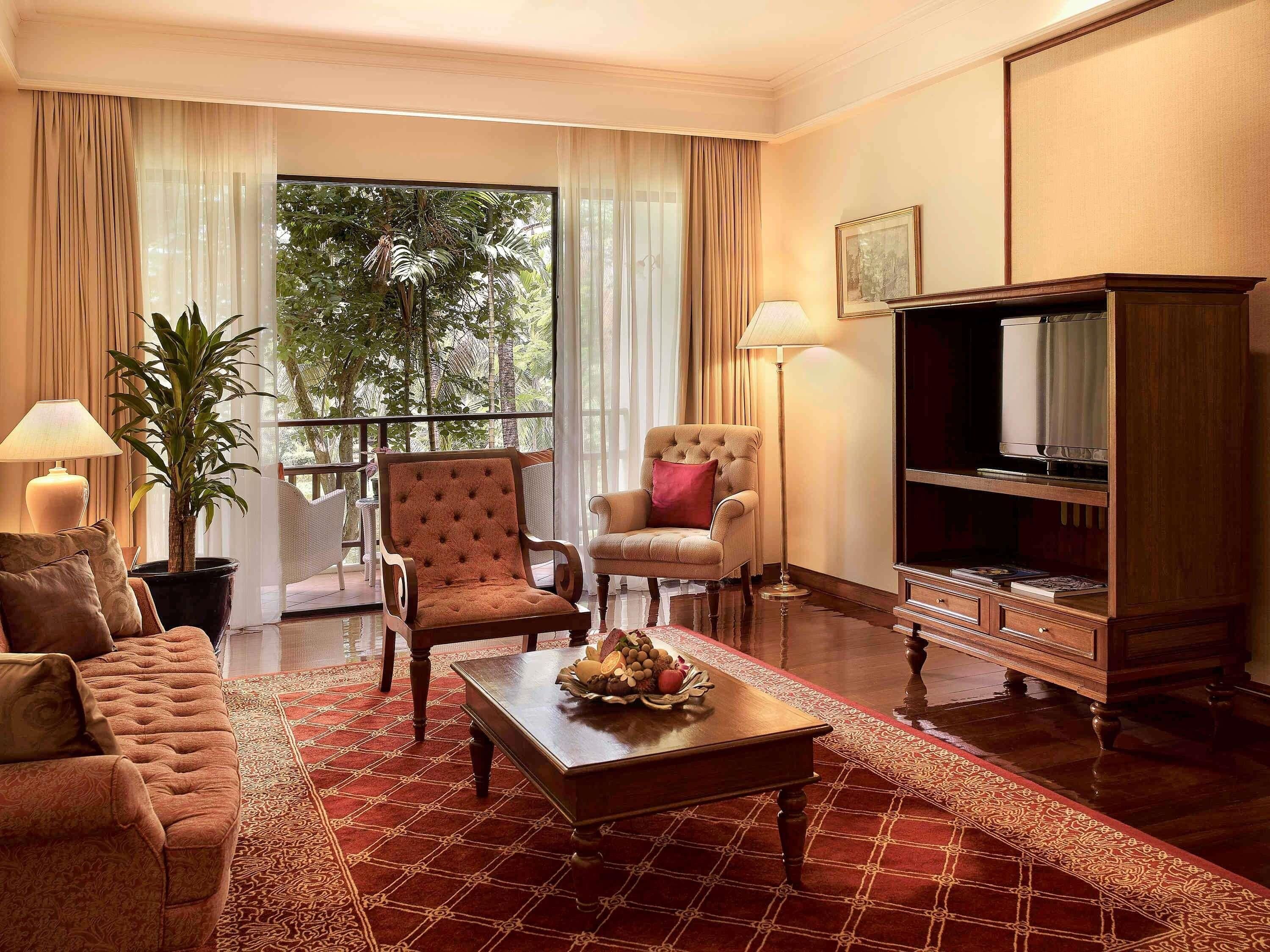 A well-furnished living room with a sofa, two armchairs, a coffee table, a television, and a potted plant.