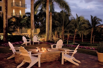 A golf course with a pool, palm trees, and a building with a red roof. at The Ritz-Carlton Naples, Tiburon