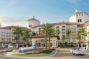 A hotel with multiple floors, palm trees, and a fountain in the courtyard.