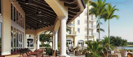 An outdoor patio area with multiple seating arrangements, including tables and chairs, and a pool in the background.