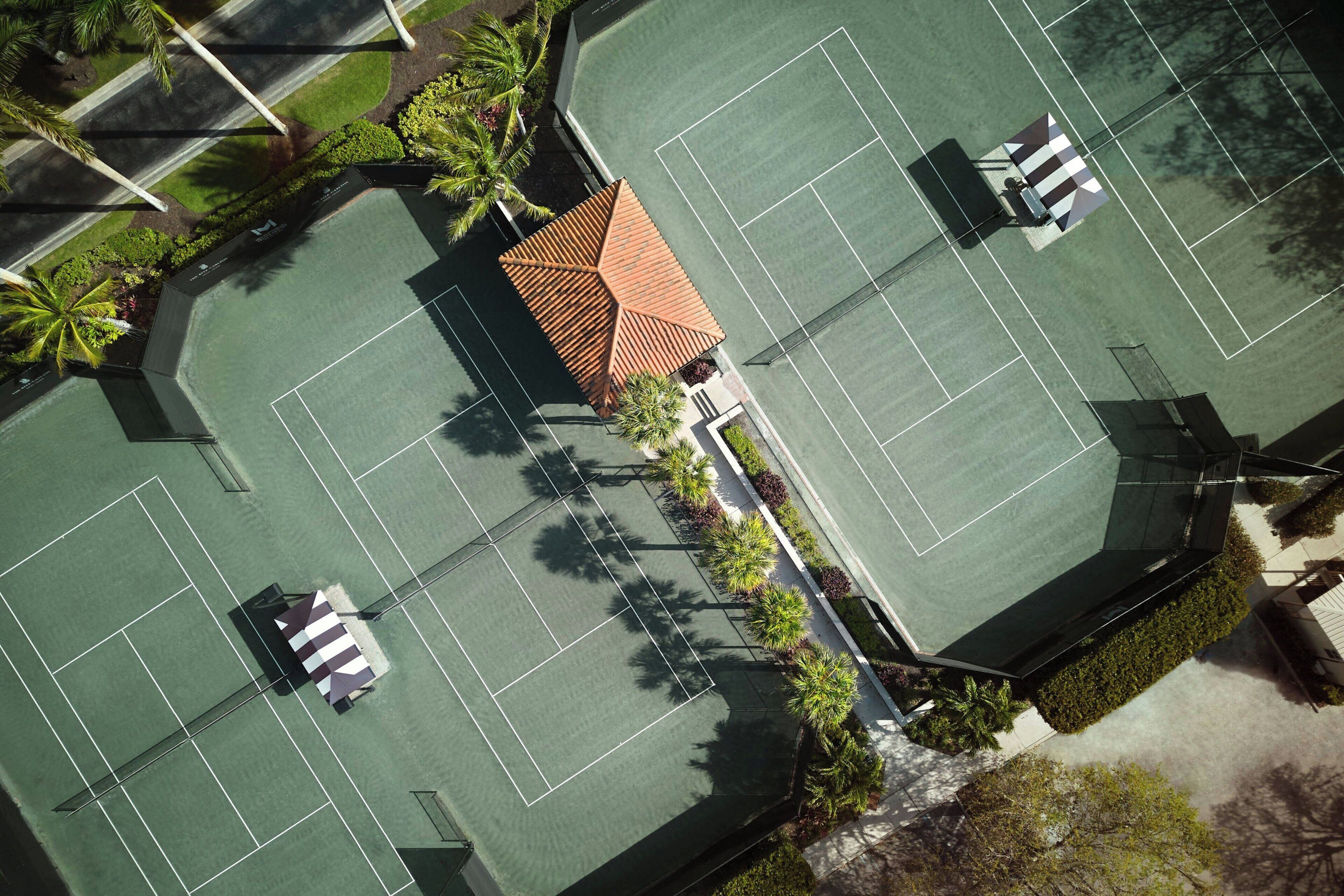 Vue aérienne d’un complexe de courts de tennis comprenant plusieurs terrains, un bâtiment central et des espaces verts environnants.