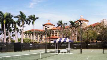 Un court de tennis avec un filet, un banc et un pavillon doté d’une marquise à rayures.