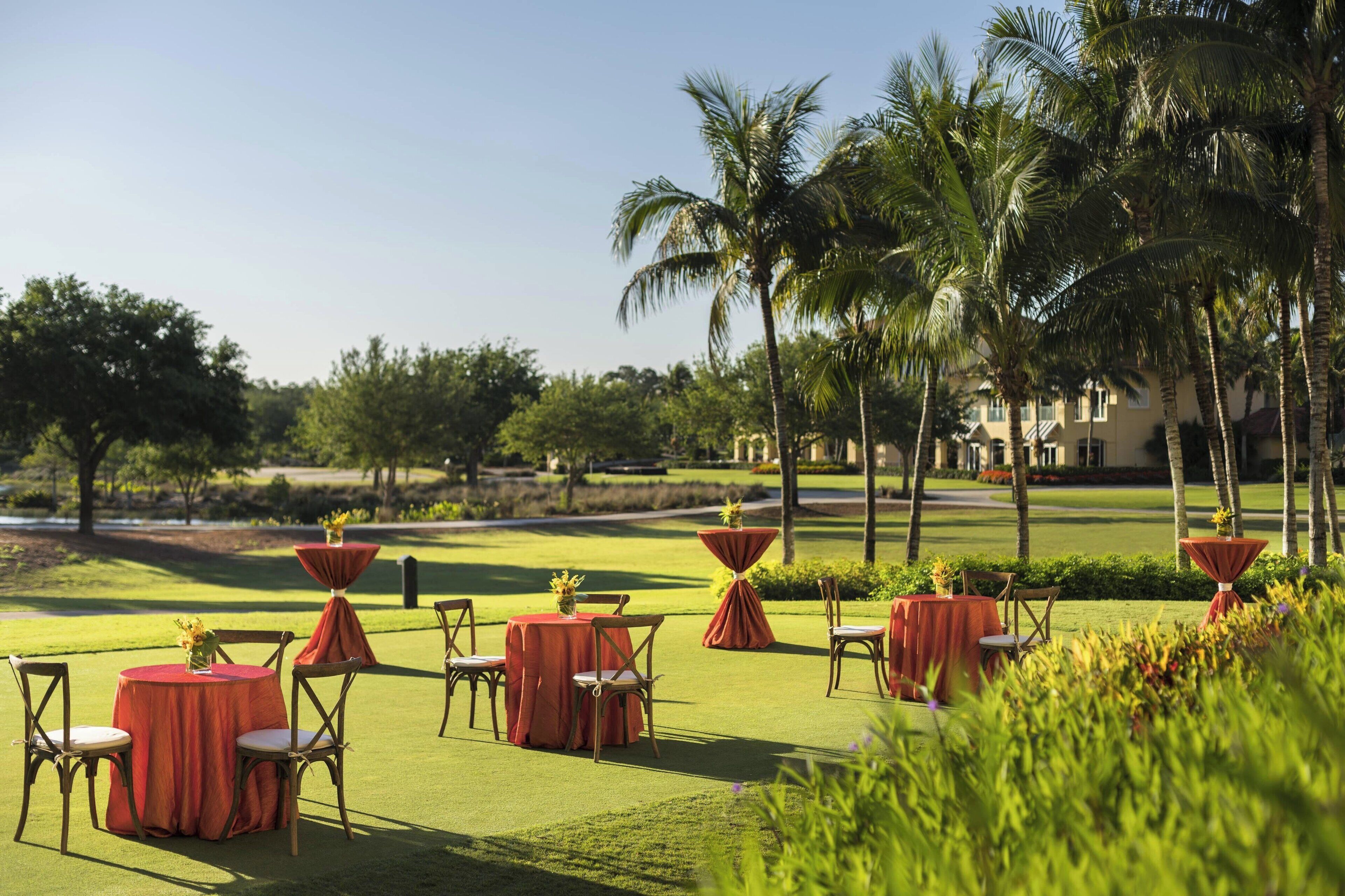 Campo de golf con mesas y sillas dispuestas para un evento, rodeado de palmeras y follaje.