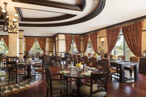 A spacious dining area with multiple tables set for dining, featuring a mix of wooden and upholstered chairs.