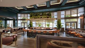 A spacious bar area with multiple seating options, including bar stools and cushioned chairs, surrounded by large windows and indoor plants.