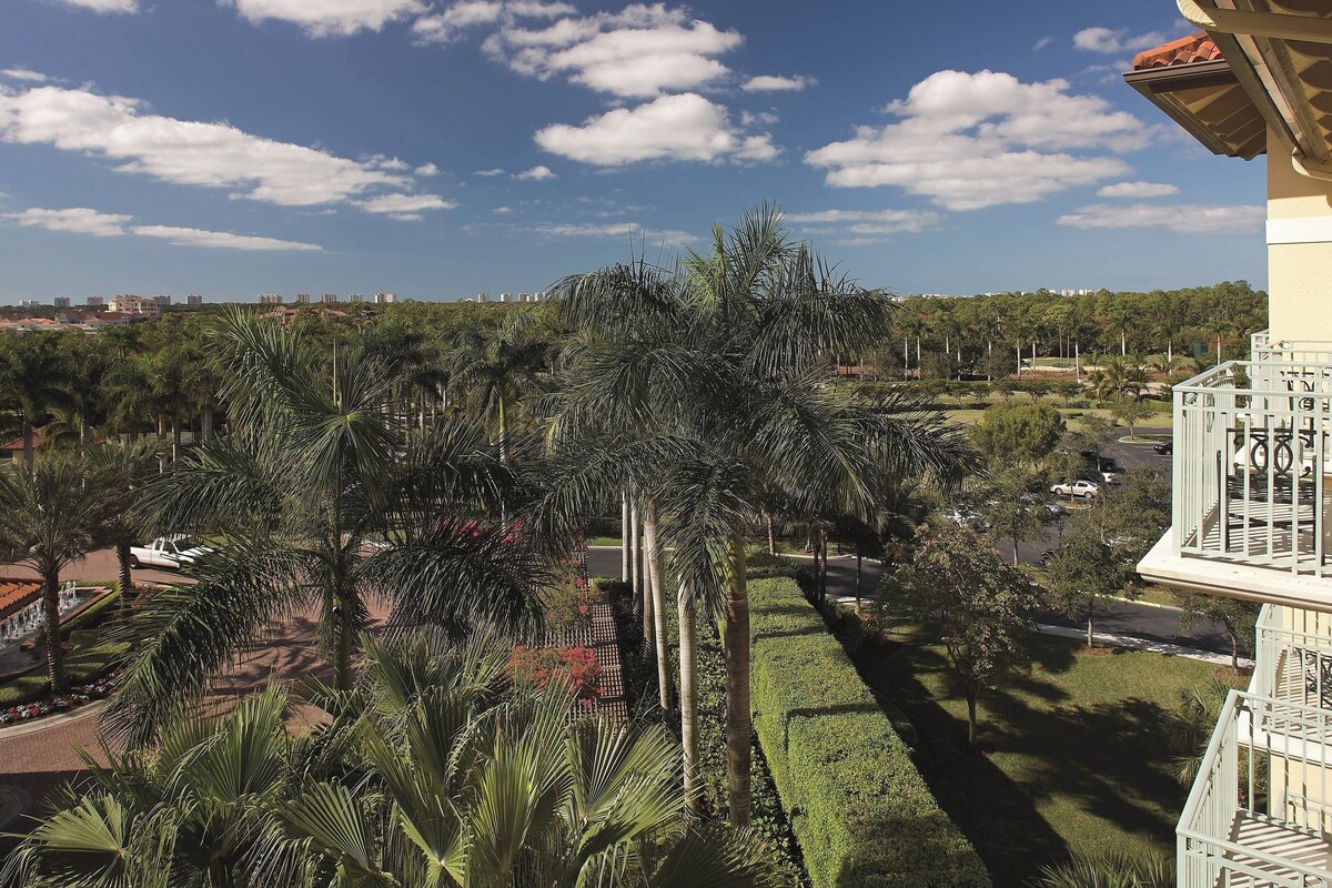 A view of a landscaped area with palm trees and a building with a balcony.