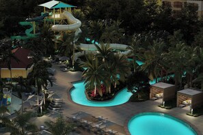 Zona de piscina en un resort con tobogán de agua, sillas de descanso y palmeras.