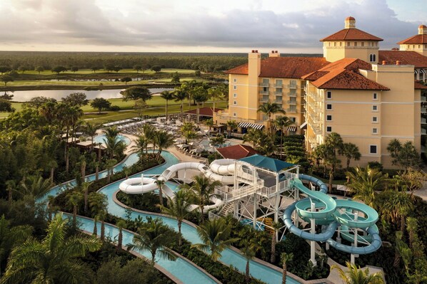 A resort with a water park, including slides and a pool area, surrounded by palm trees and a golf course in the background.