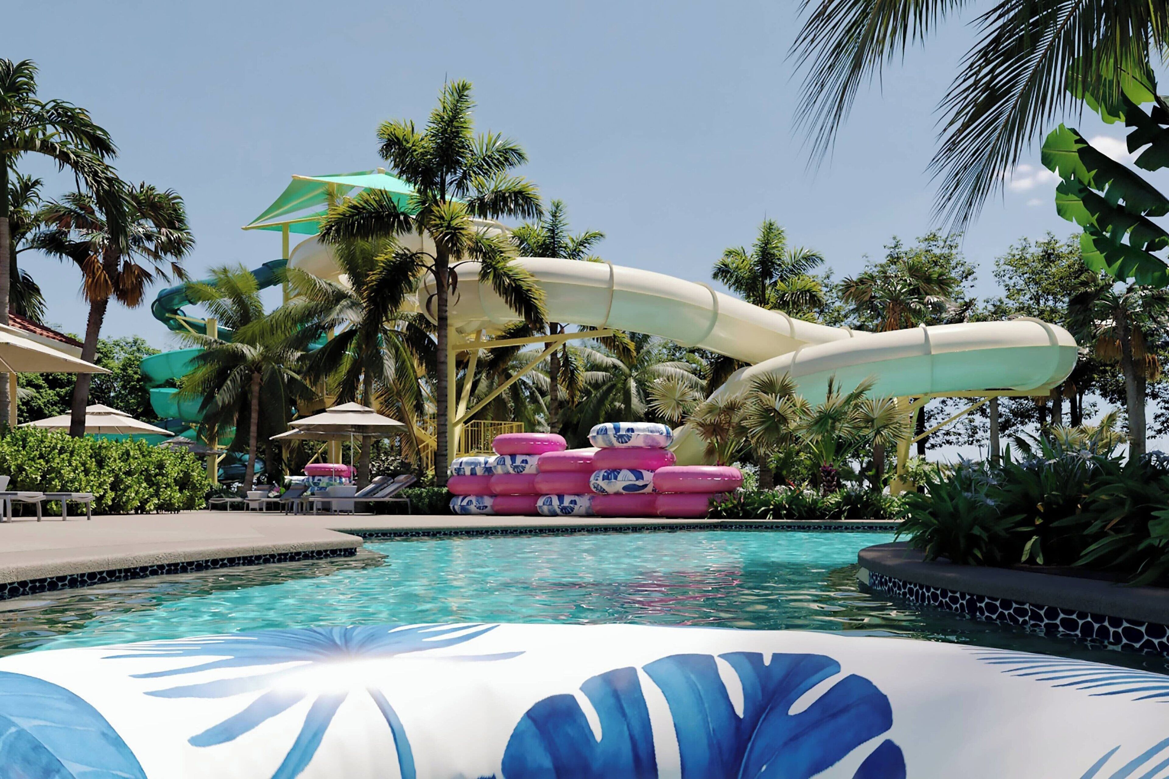 Un espace piscine doté d’un toboggan, de chaises longues et de palmiers.