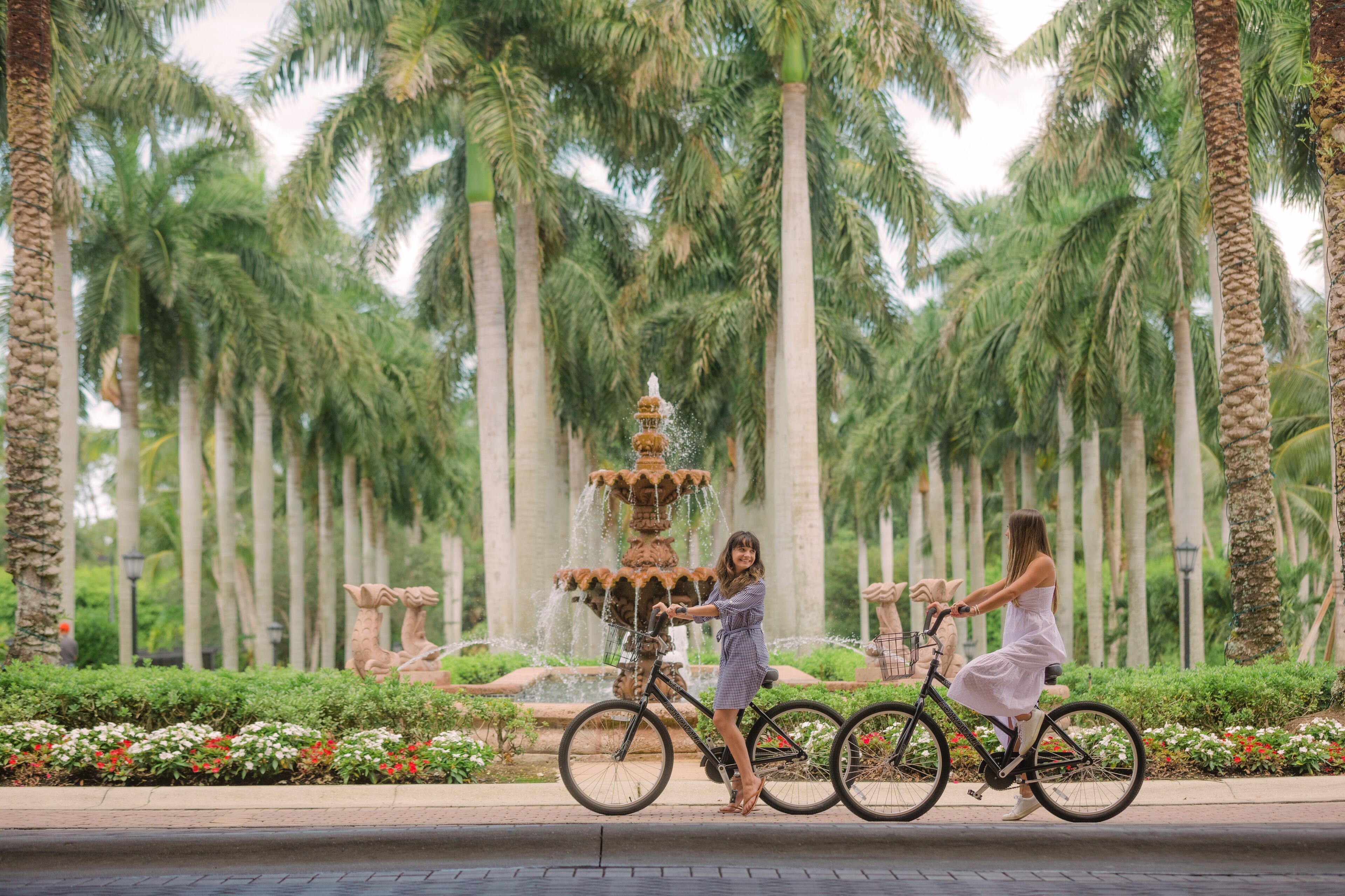 Una donna in bicicletta in un parco con una fontana e palme.