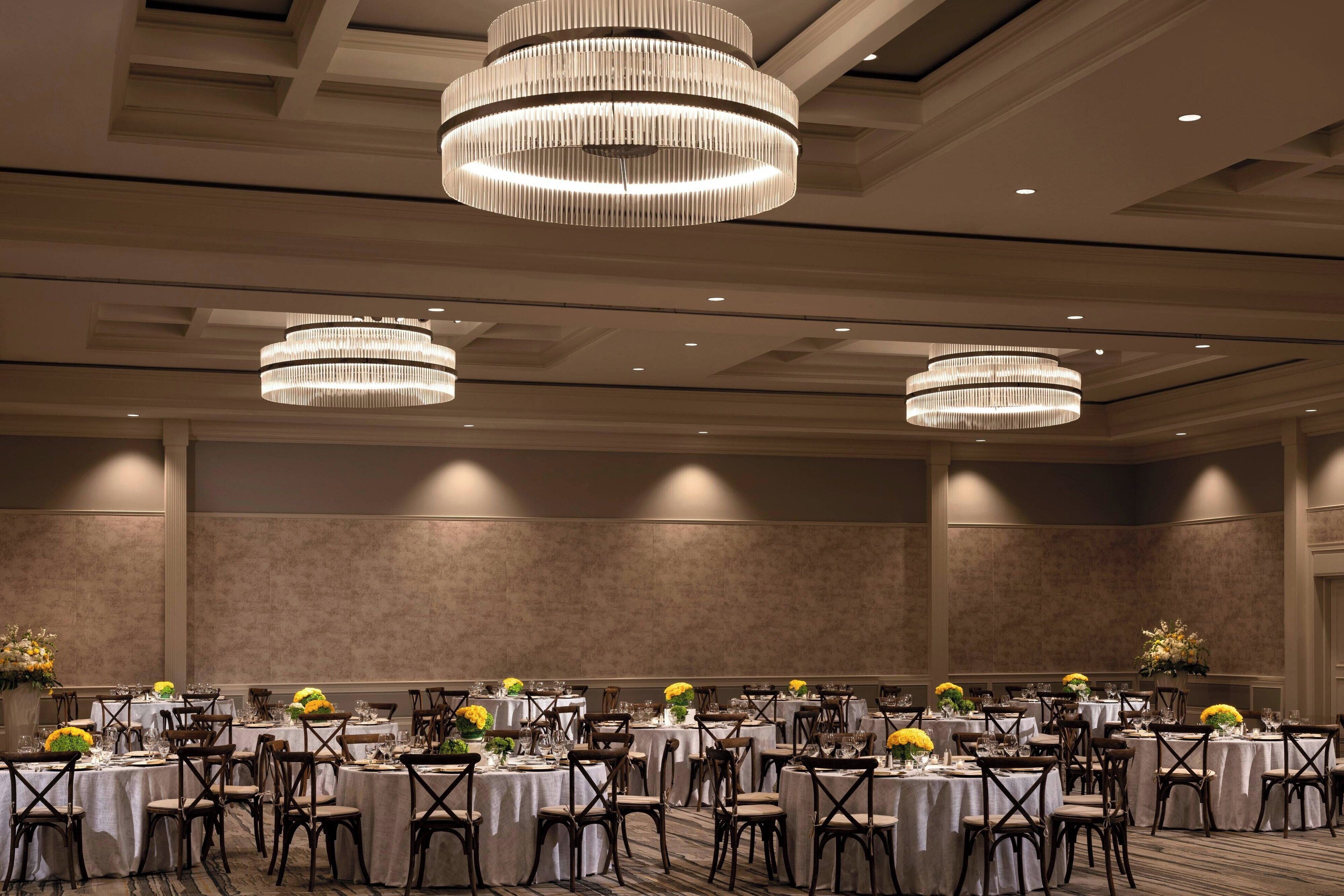 Une salle de banquet avec des tables rondes, des chaises, des lustres et des compositions florales en guise de décoration centrale.