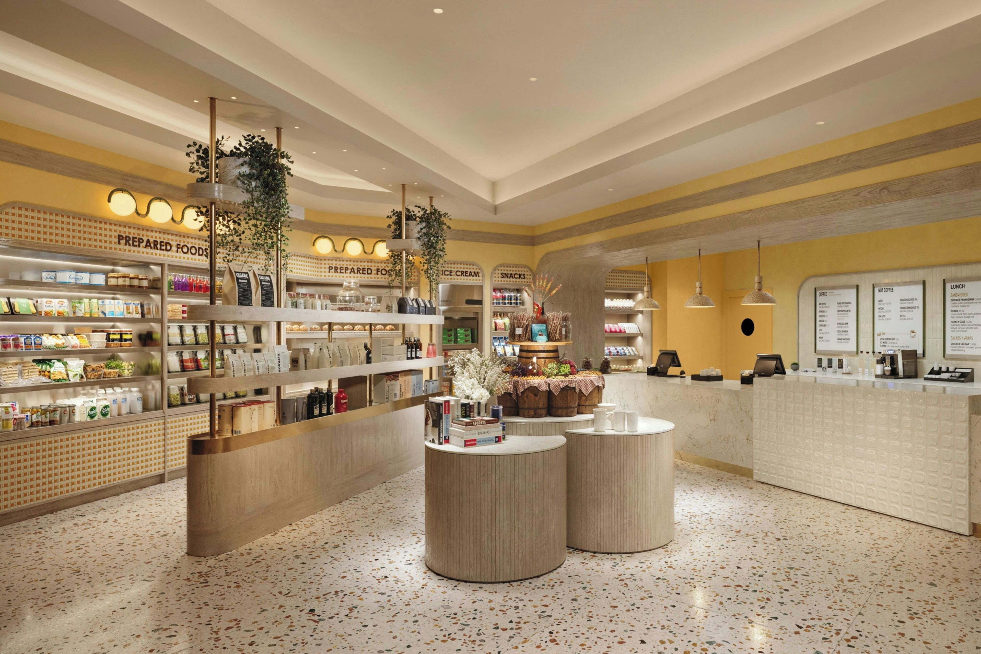 L'intérieur d'un café moderne présente un îlot central, des étagères remplies de produits alimentaires et un comptoir avec un menu.