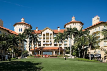 An outdoor seating area with Adirondack chairs around a stone fire pit, palm trees, and a building with balconies in the background. at The Ritz-Carlton Naples, Tiburon