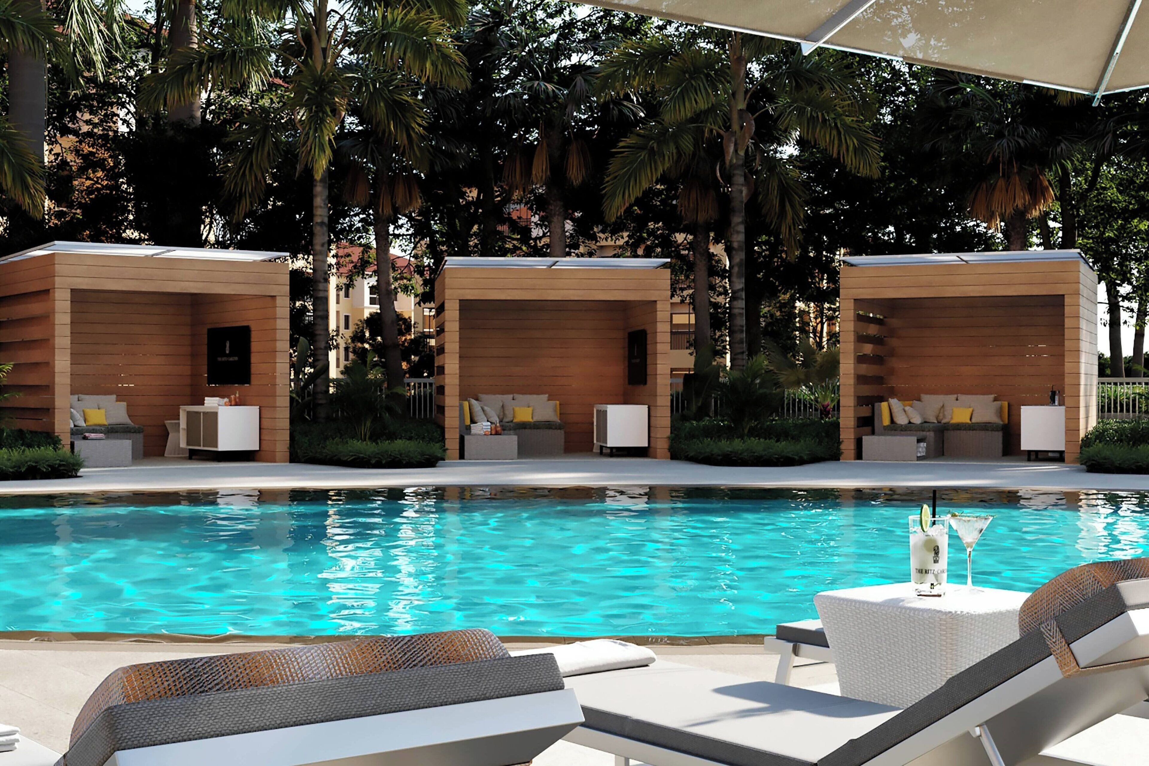 Un área junto a la piscina con tres cabañas de madera, sillas de descanso y una mesa con bebidas.