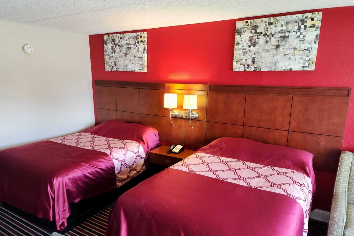 A hotel room with two beds, a wooden headboard, a nightstand with a phone, and two wall-mounted lamps.