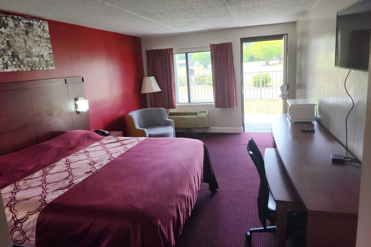 A hotel room with a bed, a desk, a chair, a television, and a window with curtains.
