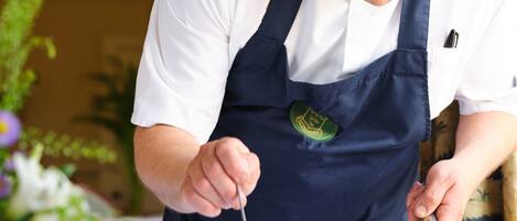 A person in a white shirt and dark apron serving food from a pot onto a plate.