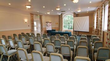 A conference room with rows of chairs, a projector screen, and a table with a blue tablecloth.