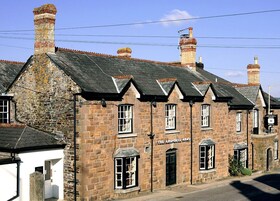 A traditional stone building with multiple chimneys, a sign reading "The Arundell Arms Hotel," and a clear blue sky in the background.