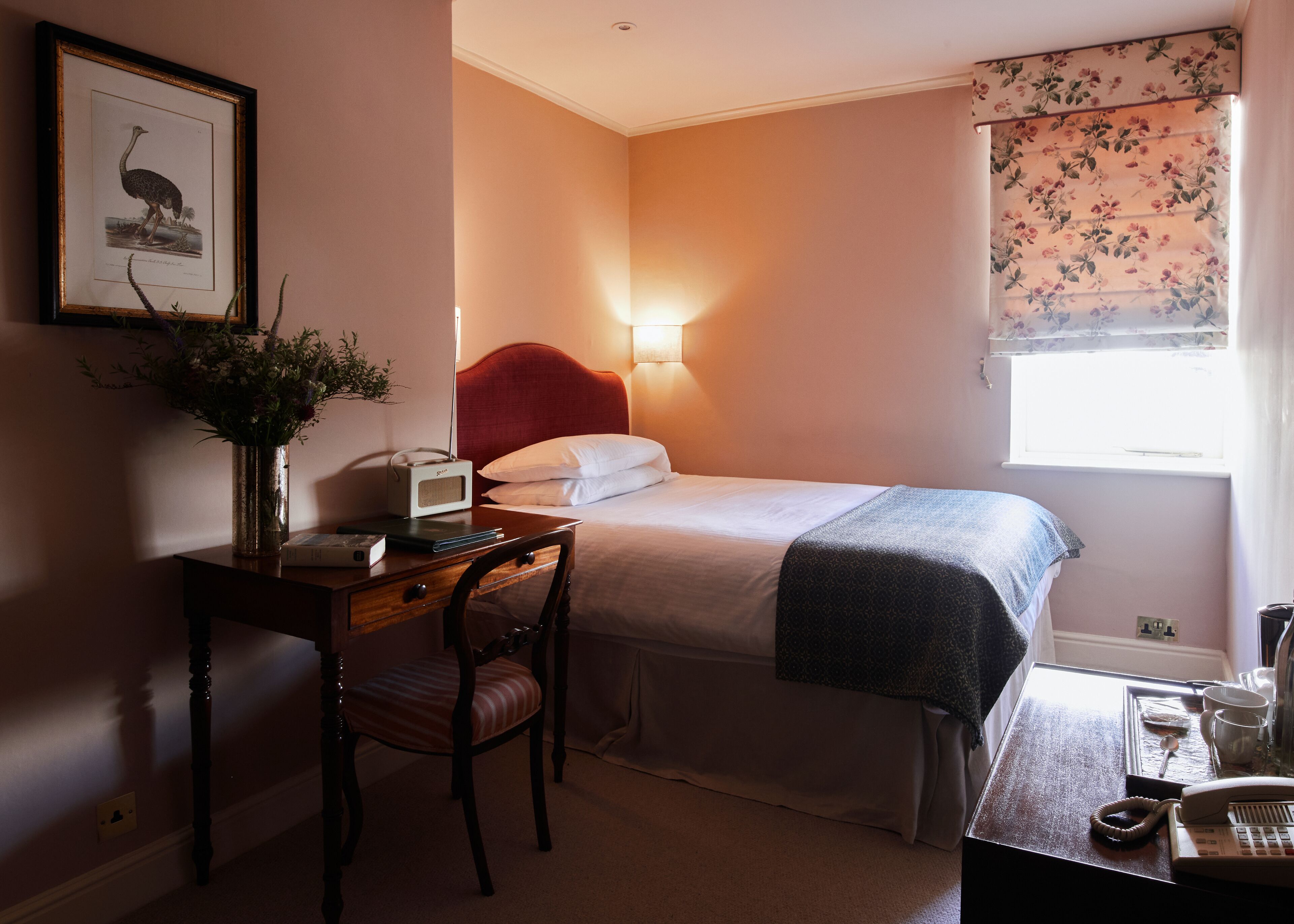 A bedroom with a bed, bedside table, chair, lamp, and a framed picture on the wall.