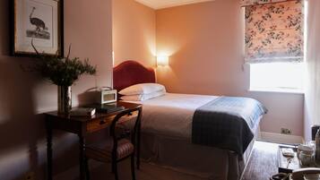 A bedroom with a bed, bedside table, chair, lamp, and a framed picture on the wall.