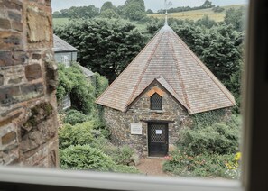 A stone building with a steeply pitched roof, surrounded by lush greenery and a sign indicating it is a craft shop. - The Arundell  (Lifton)