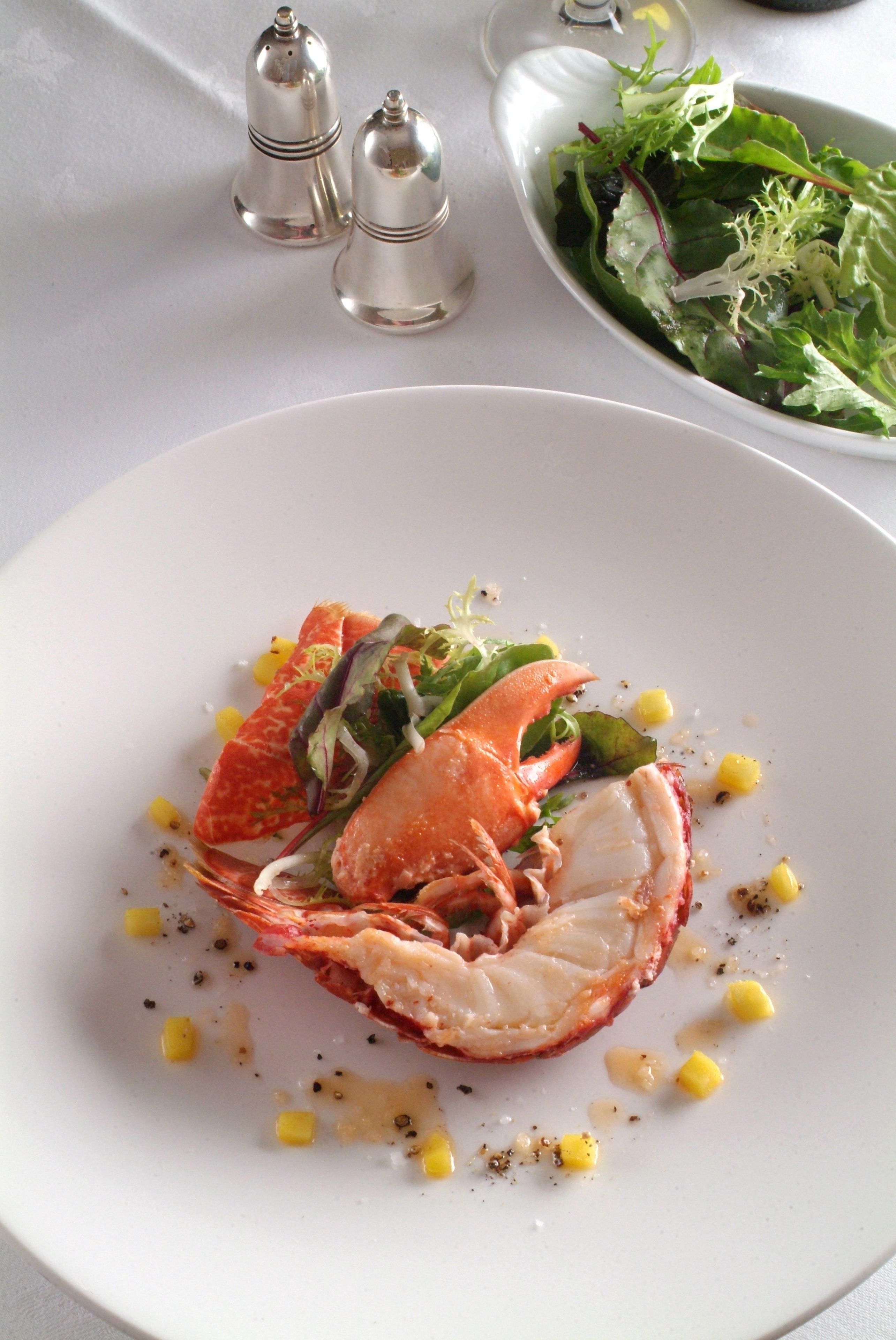 A plate with crab, corn, and greens, and a bowl of salad in the background.