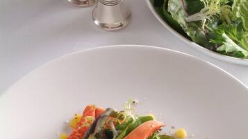 A plate with crab, corn, and greens, and a bowl of salad in the background.