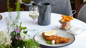 A person pouring wine into a glass, a plate with a fish dish, a basket of fries, and a small bowl of sauce on a table. - The Arundell  (Lifton)