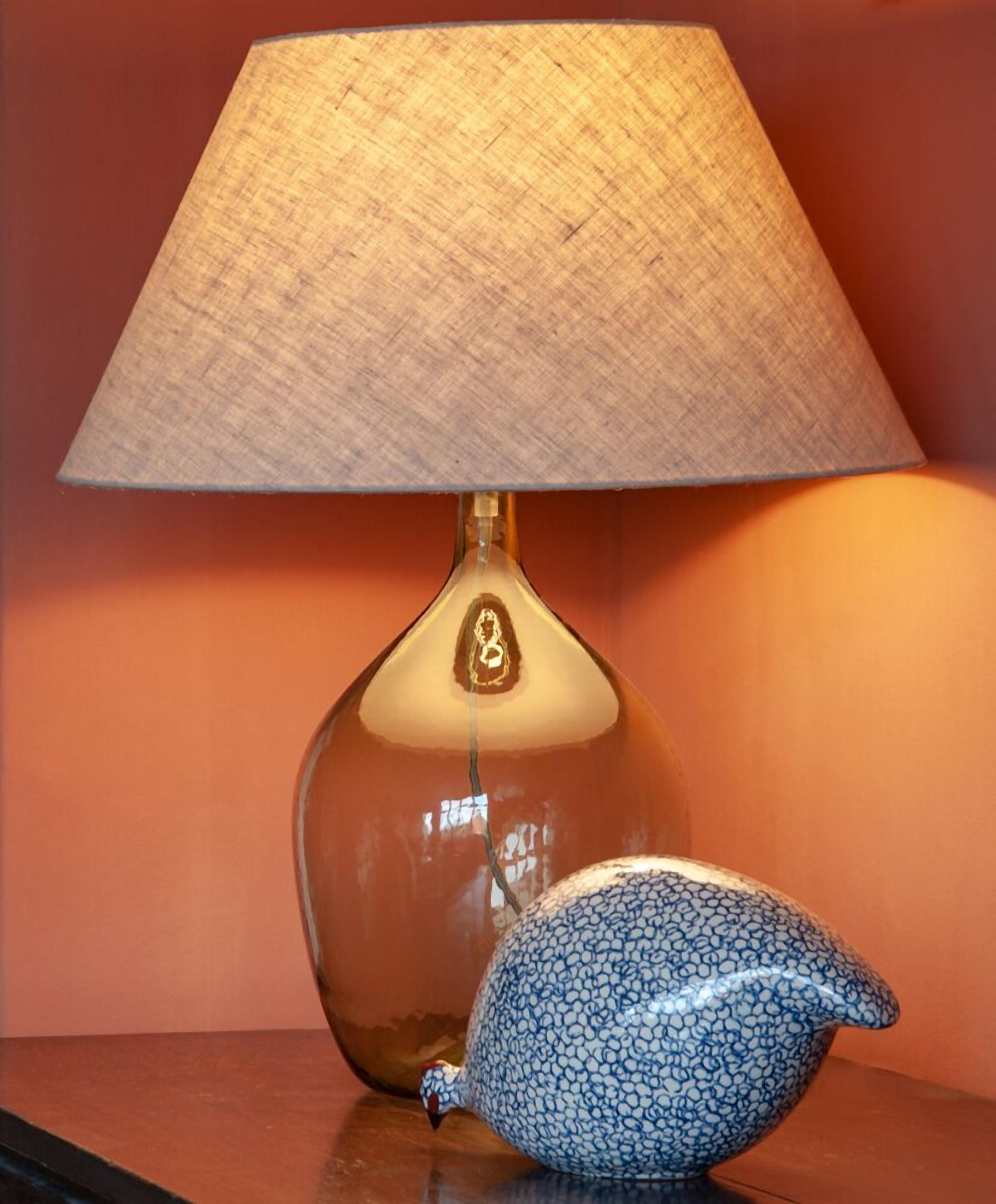 A lamp with a textured lampshade and a ceramic bird-shaped object on a wooden surface.