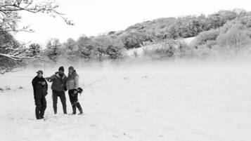 Three people standing in a snowy field with trees in the background.
