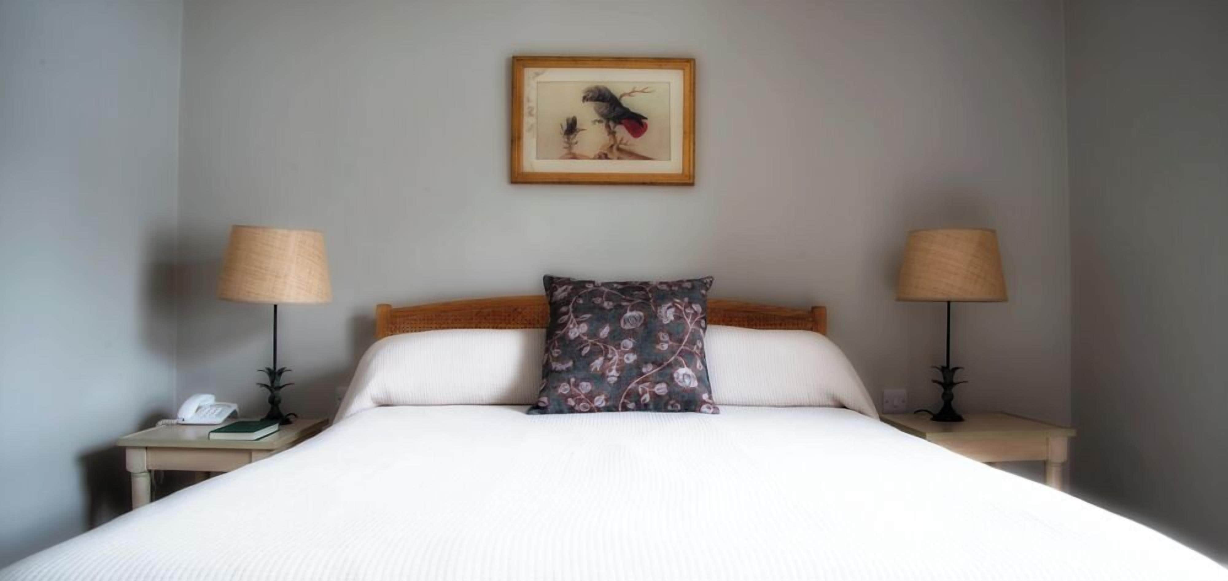 A neatly made bed with white linens, a floral pillow, and two bedside lamps on either side.