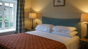 A neatly made bed with white linens, a patterned red and beige bedspread, and two bedside lamps.