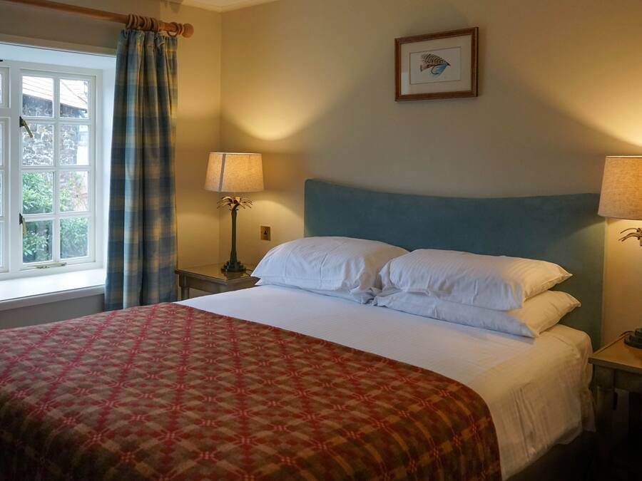 A neatly made bed with white linens, a patterned red and beige bedspread, and two bedside lamps.