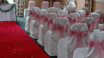 Filas de sillas blancas con lazos rosados, alfombra roja y decoración floral.