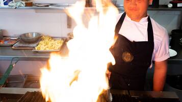 A chef cooking with a grill, surrounded by kitchen shelves with various spices and condiments.