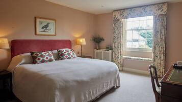 A neatly made bed with a red headboard, a bedside table with a lamp, and a window with floral curtains.