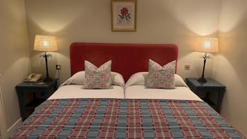Una cama doble con cabecera roja, dos almohadas estampadas, una obra de arte floral en la pared, dos mesitas de noche con lámparas y una colcha estampada.