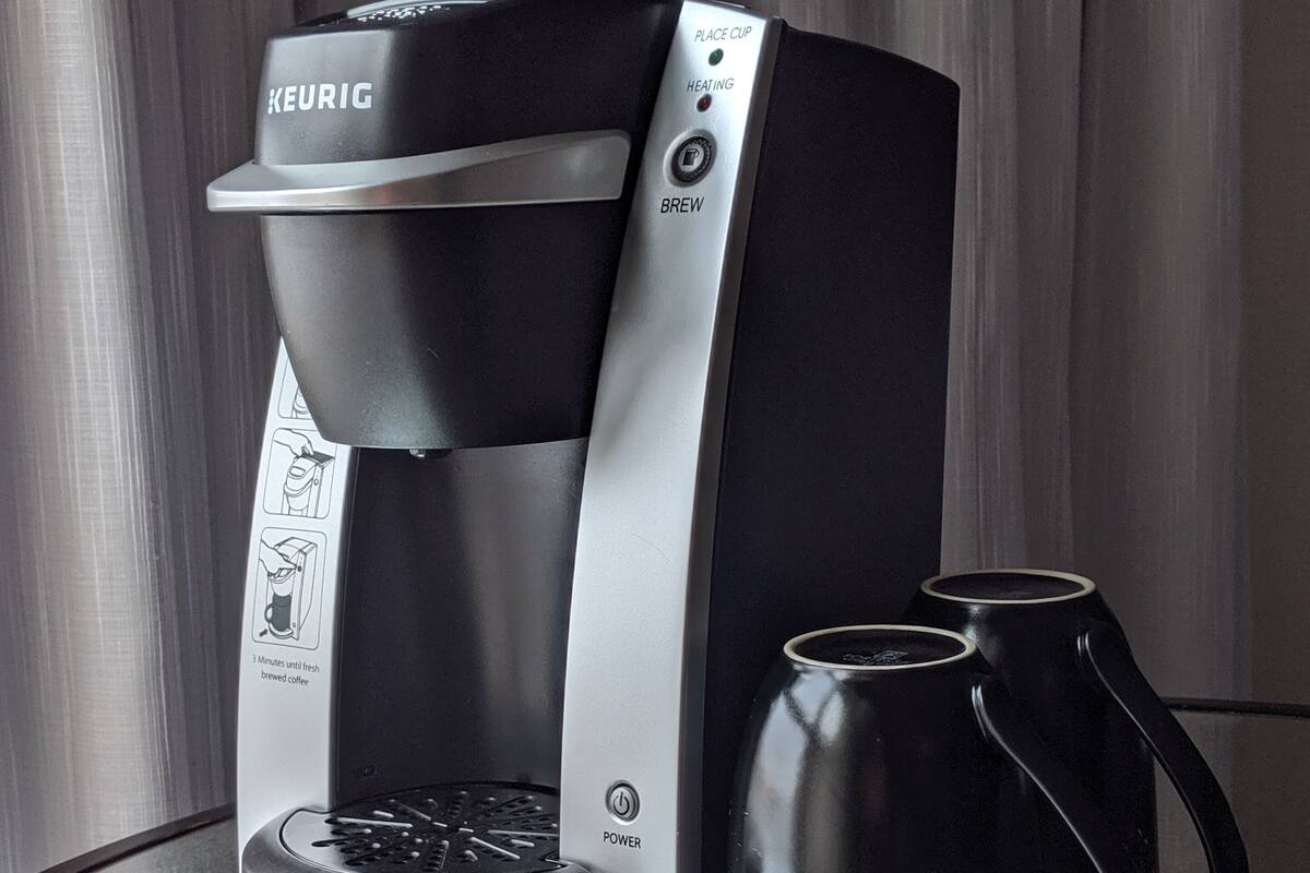 A Keurig coffee maker with two black mugs on a reflective surface.