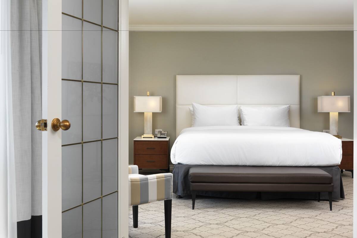A hotel room with a large bed, two bedside tables with lamps, a small chair, and a door with a modern design.