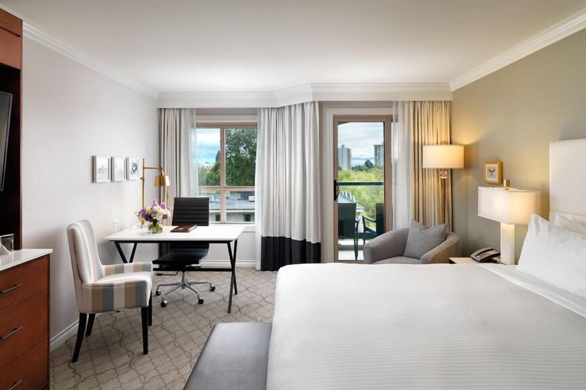 A hotel room with a bed, desk, chair, and a view of the outdoors.