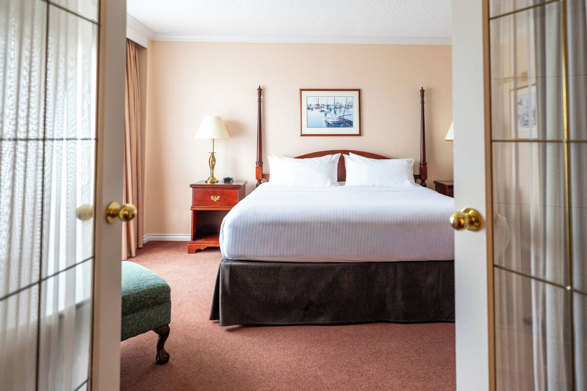 A hotel room with a bed, a nightstand, a lamp, a framed picture on the wall, and a door with a curtain.