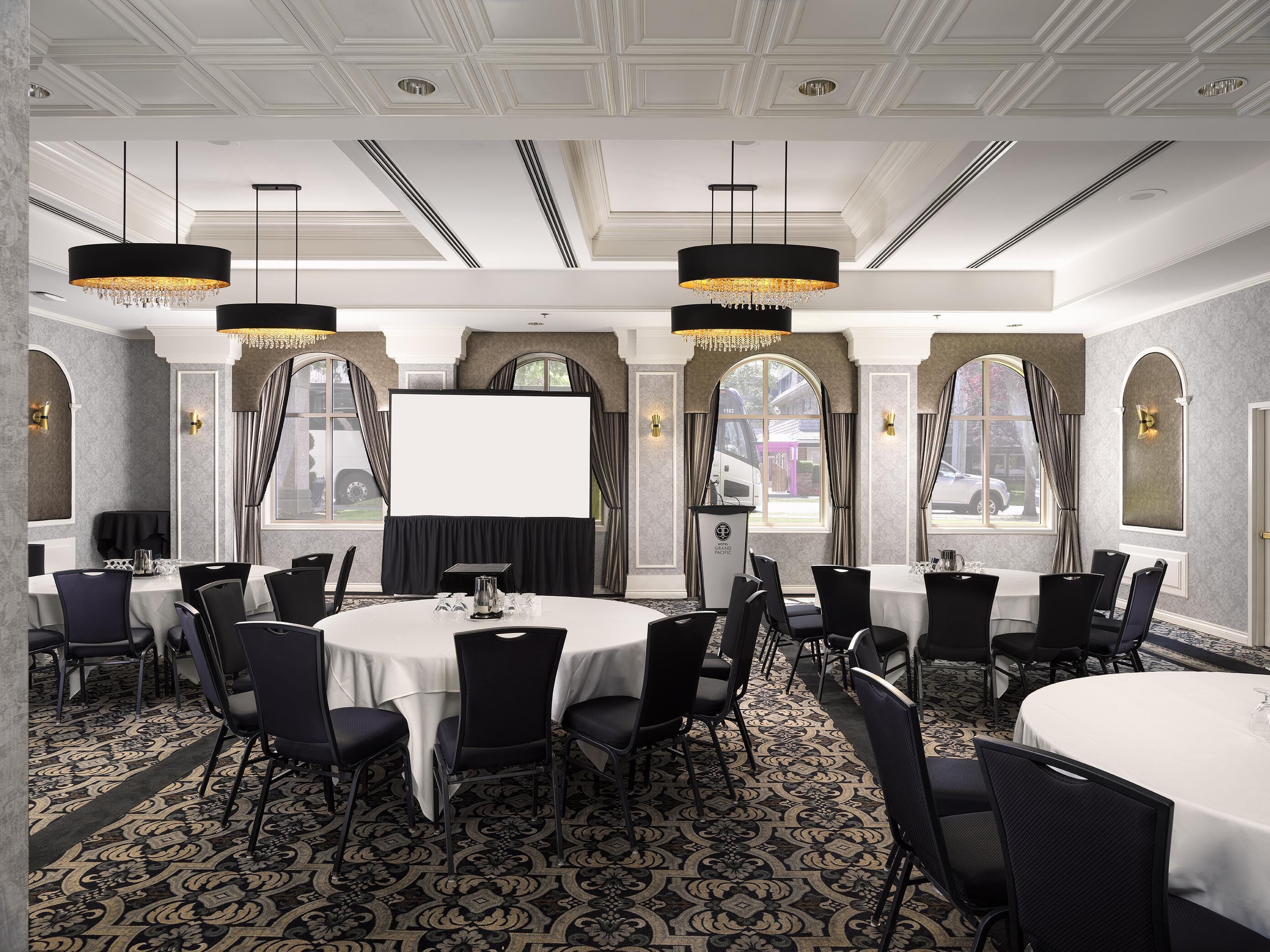 Une salle de conférence avec des tables rondes, des chaises noires, des lustres et un grand écran.