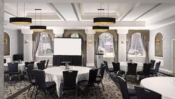Une salle de conférence avec des tables rondes, des chaises noires, des lustres et un grand écran.