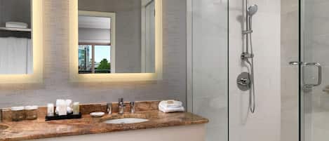 A modern bathroom with a glass shower enclosure, a large mirror, and a granite countertop with a sink and vanity.