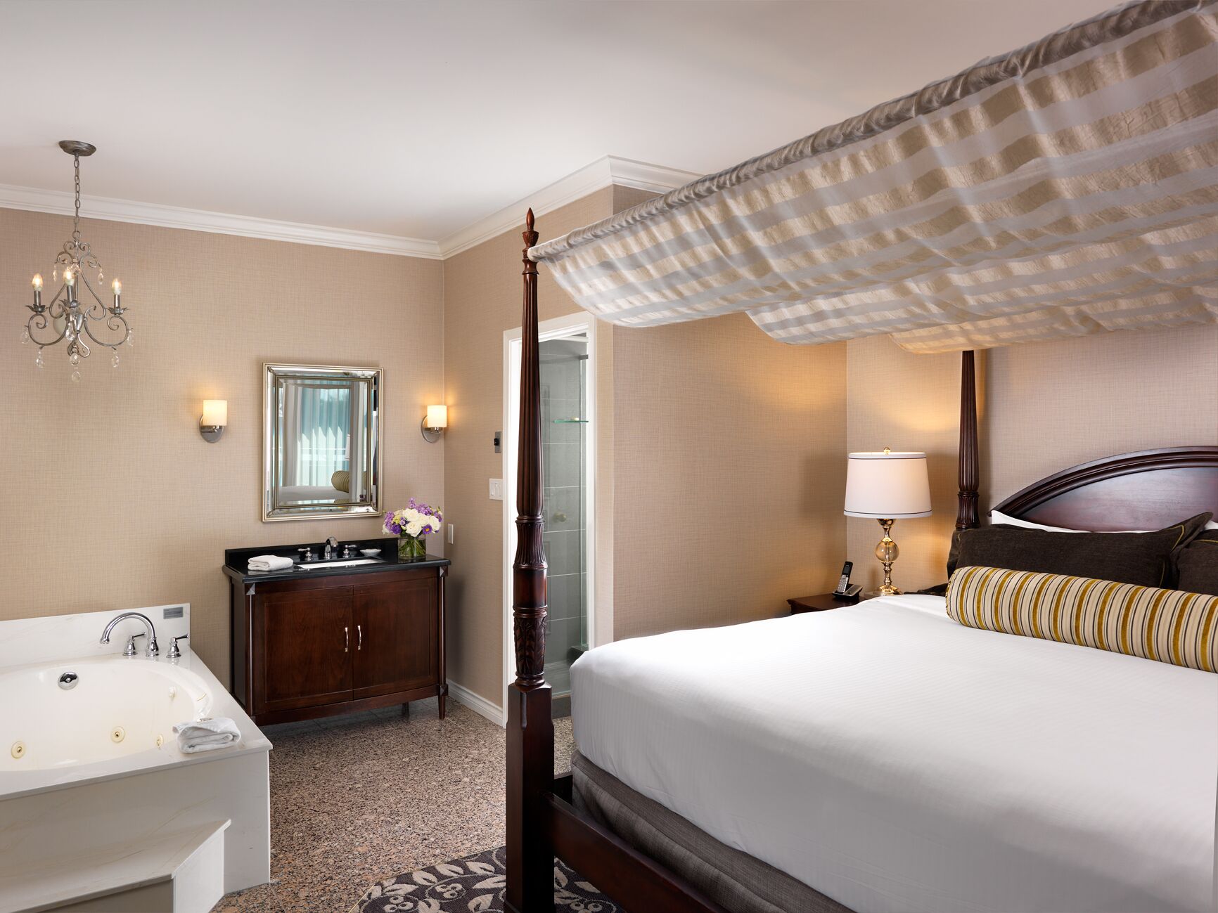 A hotel room with a large bed, a separate bathroom with a bathtub, a vanity with a mirror, and a chandelier.